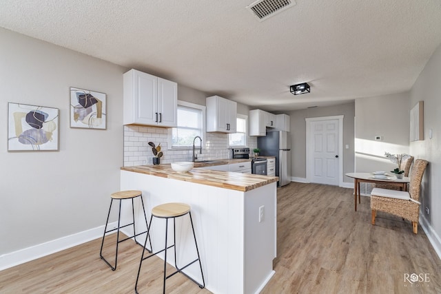 kitchen featuring sink, butcher block counters, white cabinets, a kitchen bar, and kitchen peninsula