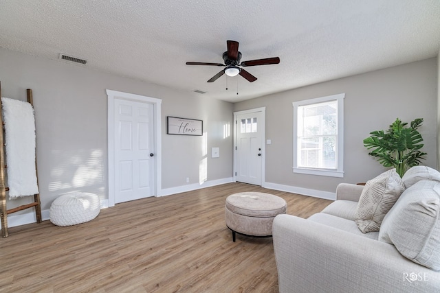 living room featuring ceiling fan, a textured ceiling, and light wood-type flooring