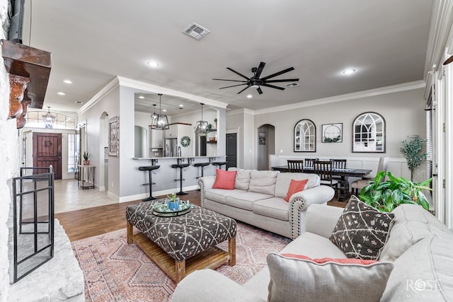 living room with wood finished floors, visible vents, recessed lighting, arched walkways, and ornamental molding