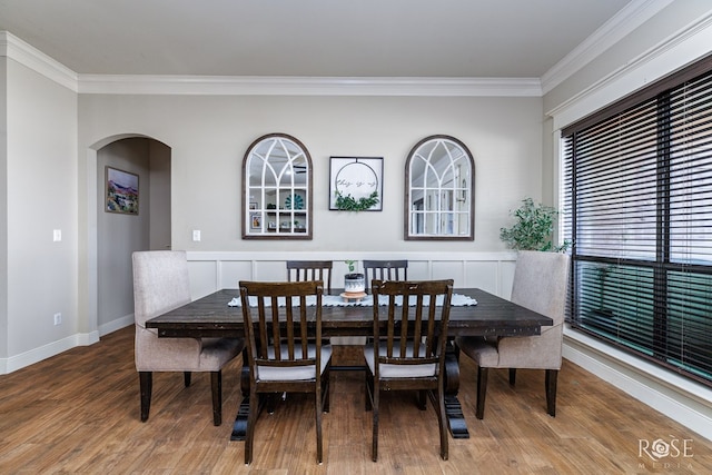 dining space featuring arched walkways, crown molding, baseboards, and wood finished floors