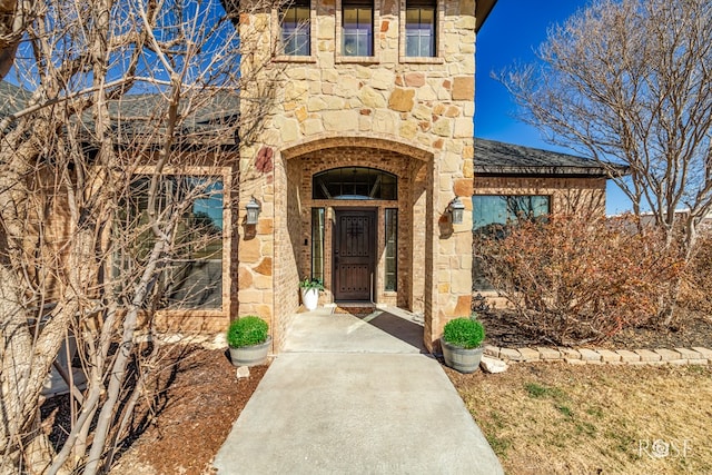 entrance to property featuring stone siding and roof with shingles