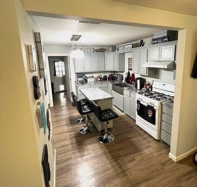 kitchen with a kitchen bar, gas range gas stove, decorative light fixtures, a center island, and dark hardwood / wood-style floors