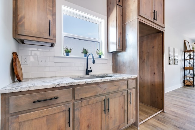 kitchen featuring sink, decorative backsplash, light stone countertops, and light wood-type flooring