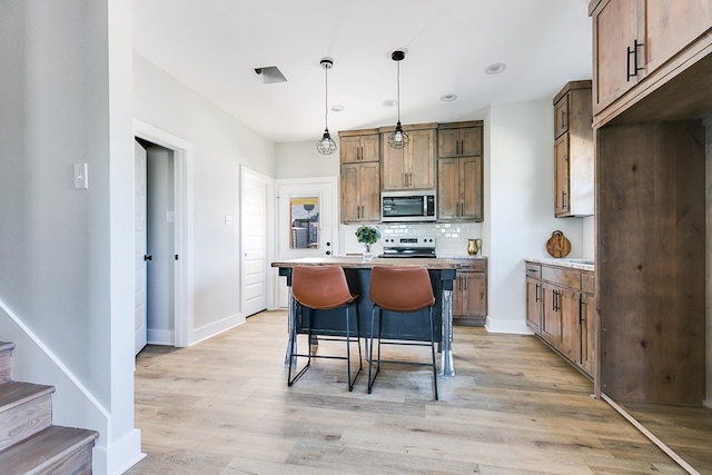 kitchen featuring decorative light fixtures, tasteful backsplash, a kitchen breakfast bar, light hardwood / wood-style floors, and stainless steel appliances