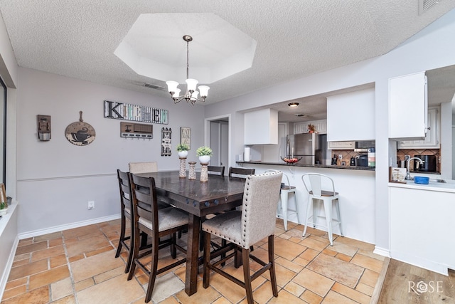 dining room featuring an inviting chandelier, sink, a raised ceiling, and a textured ceiling