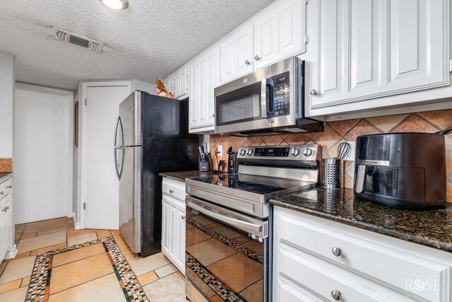 kitchen featuring white cabinetry, a textured ceiling, appliances with stainless steel finishes, dark stone counters, and decorative backsplash