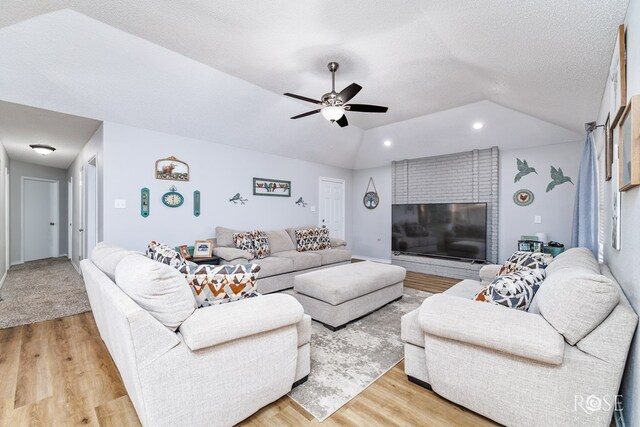 living room with ceiling fan, lofted ceiling, a textured ceiling, and light wood-type flooring