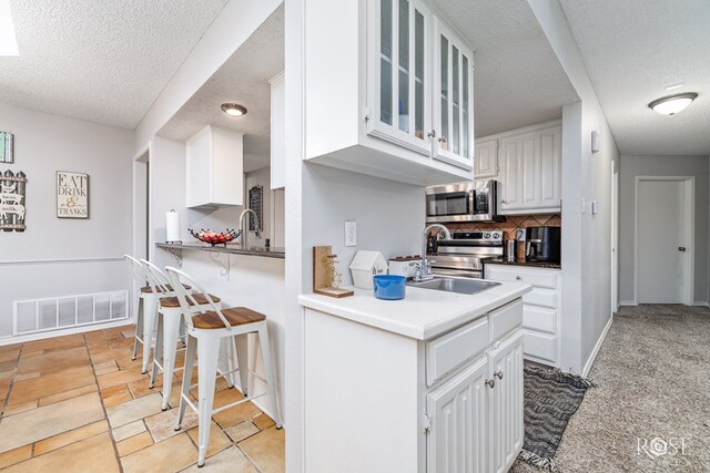 kitchen with appliances with stainless steel finishes, a breakfast bar, tasteful backsplash, white cabinets, and kitchen peninsula