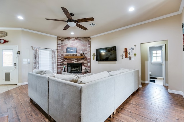 living room featuring visible vents, a brick fireplace, ornamental molding, dark wood-style floors, and a ceiling fan