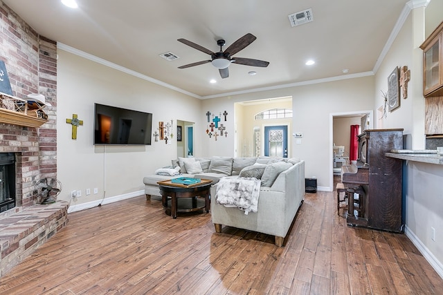 living room featuring hardwood / wood-style flooring, a brick fireplace, visible vents, and ornamental molding