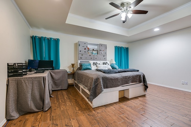 bedroom with ornamental molding, a ceiling fan, a tray ceiling, wood finished floors, and baseboards