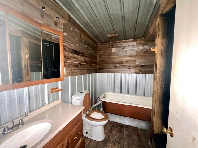 bathroom with wood walls, wood-type flooring, a tub to relax in, vanity, and toilet