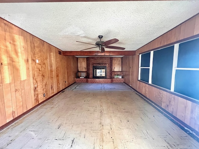 unfurnished living room with ceiling fan, a fireplace, a textured ceiling, and wood walls