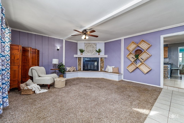 carpeted living room with beamed ceiling, ceiling fan, ornamental molding, and a tile fireplace