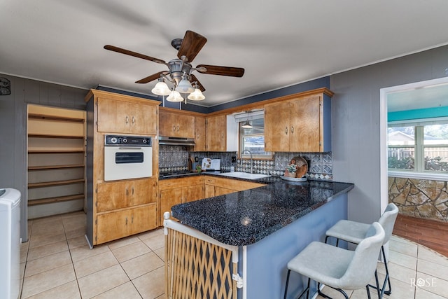 kitchen with light tile patterned flooring, kitchen peninsula, sink, and white oven