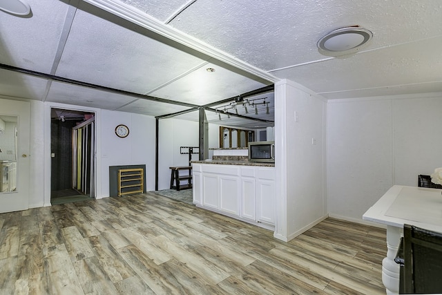interior space featuring white cabinetry, stainless steel microwave, a textured ceiling, and light wood-type flooring