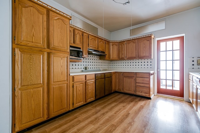 kitchen featuring brown cabinetry, backsplash, light countertops, light wood finished floors, and under cabinet range hood