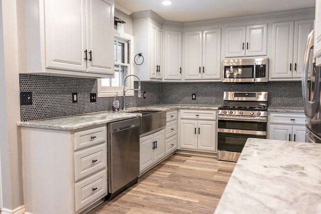 kitchen with stainless steel appliances, white cabinetry, and light stone counters