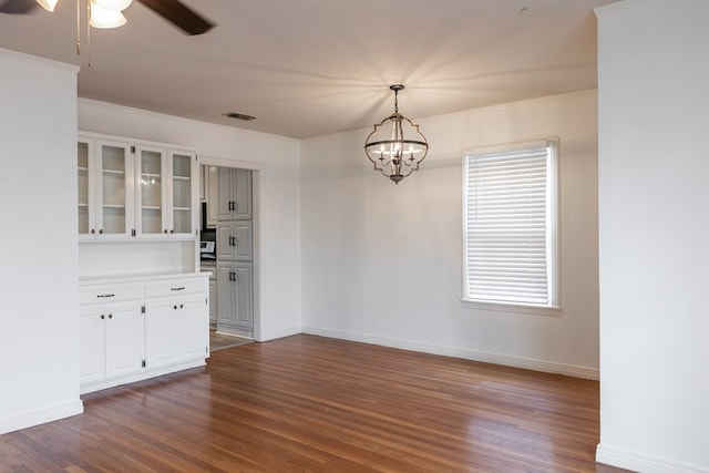 unfurnished dining area with dark hardwood / wood-style flooring, ornamental molding, and ceiling fan with notable chandelier