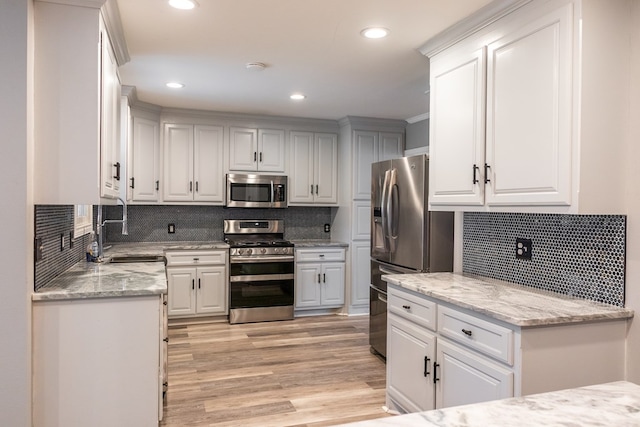 kitchen with white cabinetry, sink, stainless steel appliances, and light stone counters