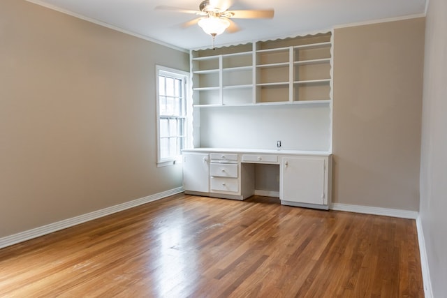 unfurnished office featuring ceiling fan, ornamental molding, built in desk, and wood-type flooring