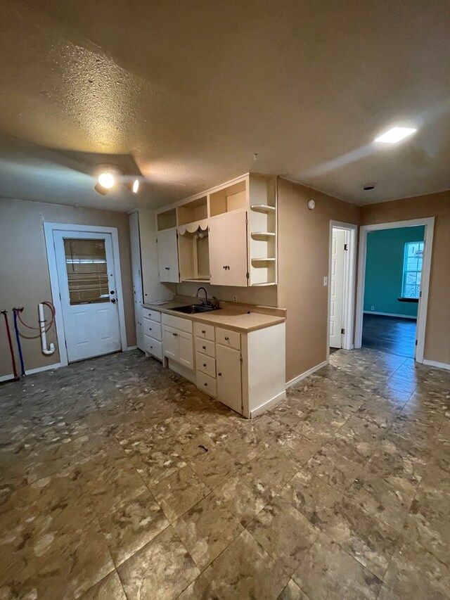 20 E 39th St, San Angelo, TX 76903 - kitchen with open shelves, white cabinetry, a sink, baseboards, and a textured ceiling