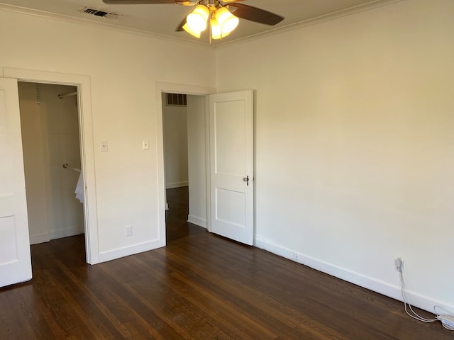 unfurnished bedroom with dark wood-type flooring, ceiling fan, ornamental molding, a walk in closet, and a closet