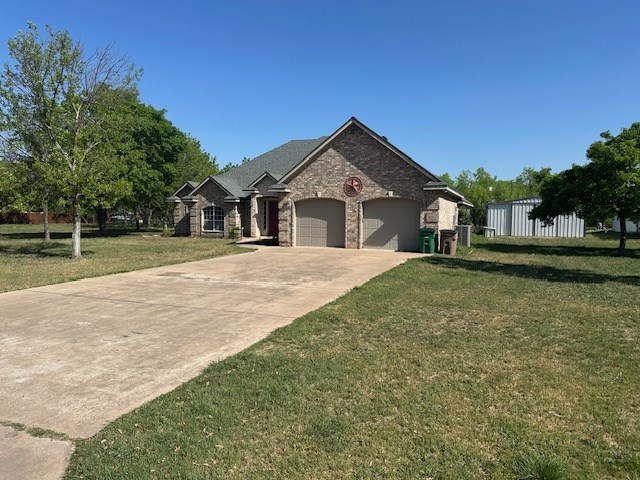 french provincial home featuring an attached garage, concrete driveway, a front yard, and brick siding