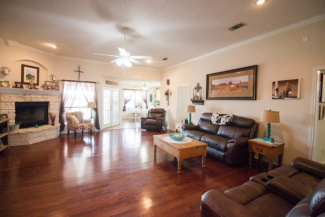 living room featuring a stone fireplace, visible vents, dark wood-style flooring, and ornamental molding