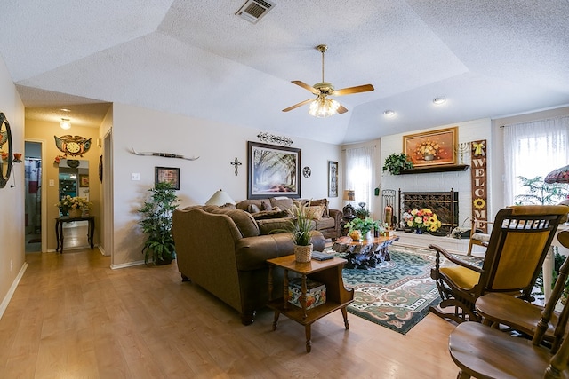 1027 Butterfly Ln, San Angelo, TX 76905 - living room with lofted ceiling, light wood-style floors, a brick fireplace, a ceiling fan, and a textured ceiling