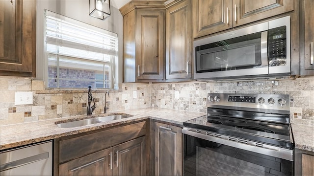 kitchen with light stone countertops, appliances with stainless steel finishes, sink, and backsplash