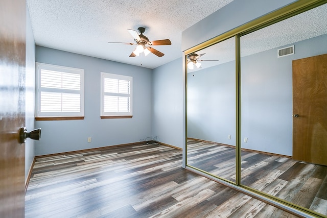 unfurnished bedroom featuring hardwood / wood-style flooring, a textured ceiling, ceiling fan, and a closet