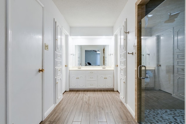 3305 Sierra Ct, San Angelo, TX 76904 - bathroom with a shower stall, wood finished floors, double vanity, a textured ceiling, and baseboards
