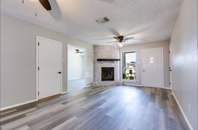 unfurnished living room featuring a textured ceiling, visible vents, a ceiling fan, wood finished floors, and a fireplace