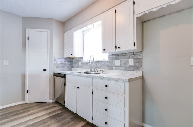 kitchen featuring tasteful backsplash, a sink, dishwasher, light countertops, and white cabinets