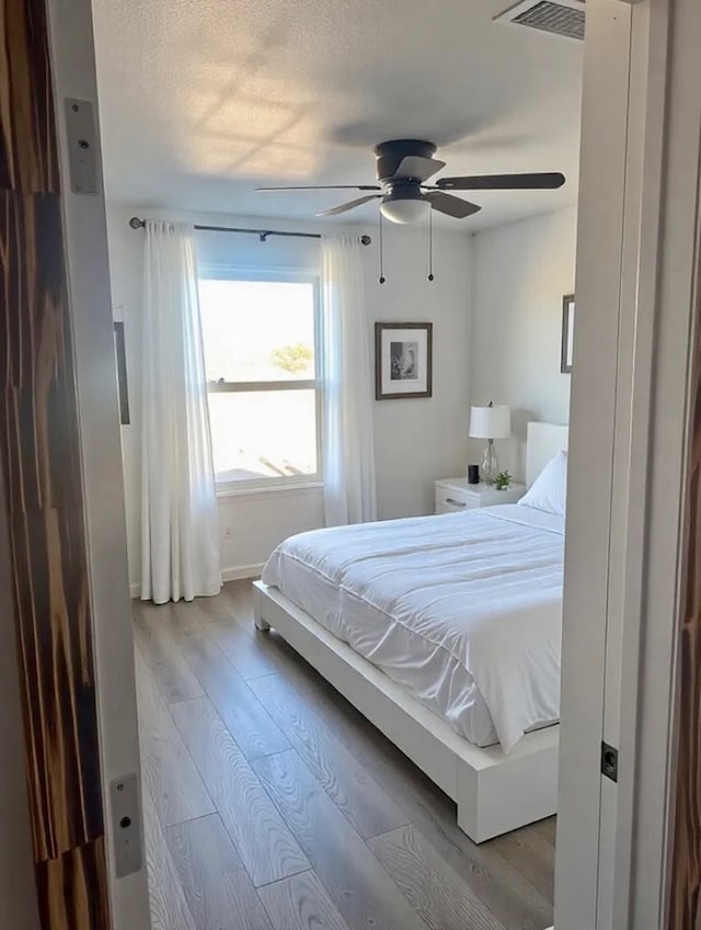 bedroom featuring baseboards, wood finished floors, visible vents, and ceiling fan