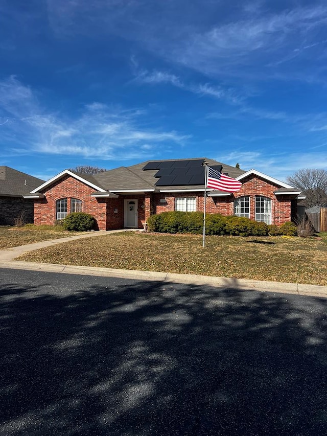 single story home with a front yard and solar panels