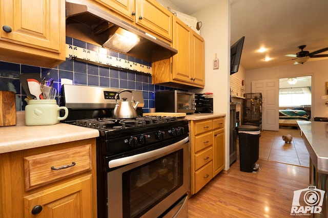 kitchen featuring extractor fan, tasteful backsplash, ceiling fan, stainless steel range with gas stovetop, and light hardwood / wood-style flooring