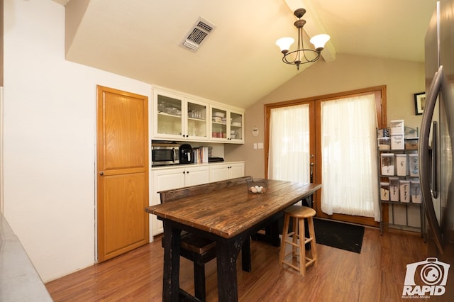 dining area with french doors, wood-type flooring, vaulted ceiling, and a notable chandelier