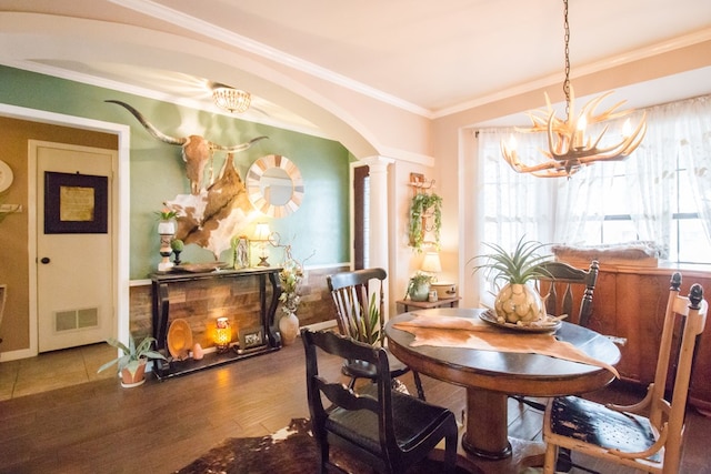 dining space featuring crown molding, a notable chandelier, visible vents, wood finished floors, and ornate columns