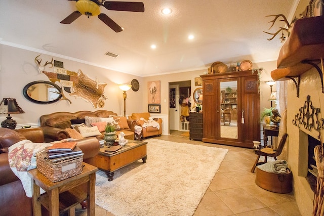 living area featuring light tile patterned flooring, a fireplace, a ceiling fan, visible vents, and crown molding