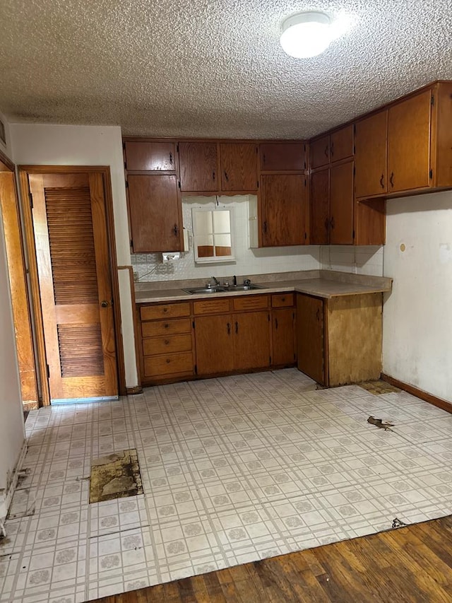 kitchen featuring decorative backsplash, light countertops, brown cabinets, a sink, and a textured ceiling