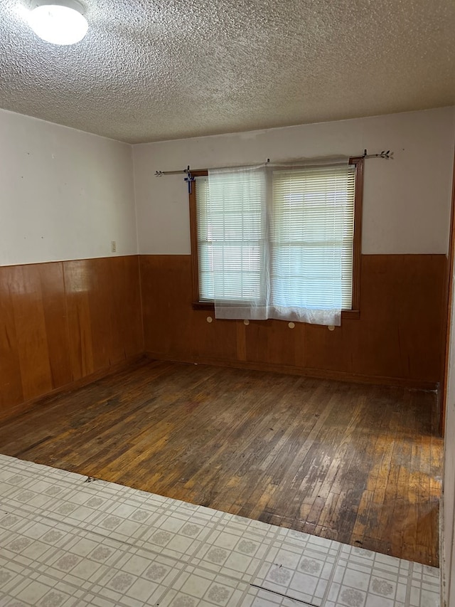 spare room featuring wood-type flooring, a textured ceiling, wainscoting, and wood walls
