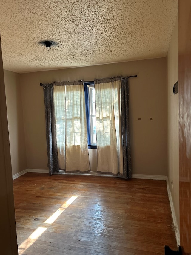 empty room with a textured ceiling, wood finished floors, and baseboards