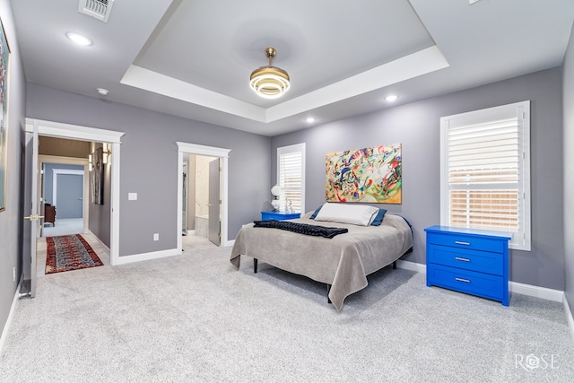 bedroom with light colored carpet, a raised ceiling, visible vents, and baseboards