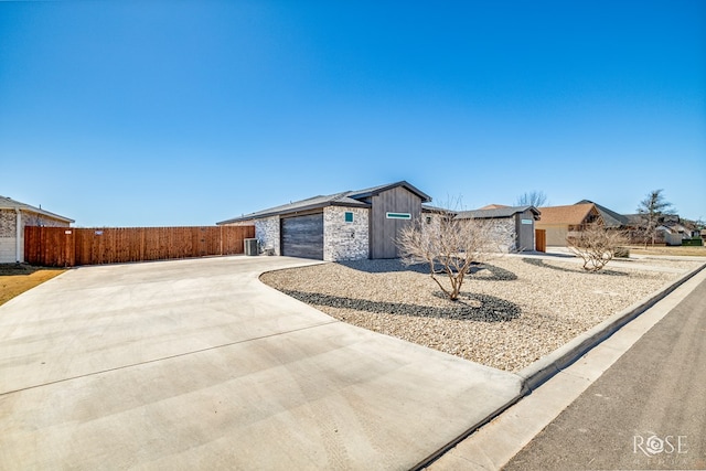 view of front facade featuring central air condition unit, fence, stone siding, concrete driveway, and board and batten siding