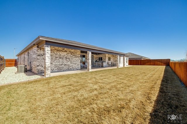 rear view of property featuring brick siding, a yard, central AC, a patio area, and a fenced backyard