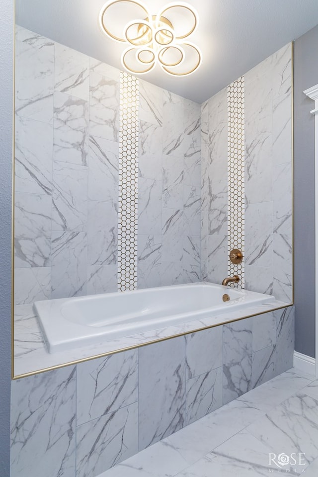 full bathroom with marble finish floor, tiled tub, and stone wall