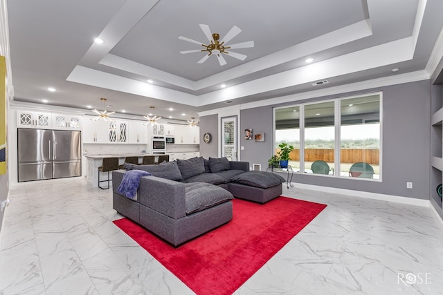 living room with visible vents, a tray ceiling, a ceiling fan, and baseboards