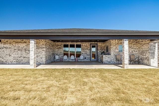 back of house featuring a yard, brick siding, and a patio